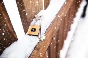 chiave della casa su una staccionata di legno in inverno nella neve. un regalo per capodanno, natale. costruzione, progettazione, progetto, trasloco in nuova casa, mutuo, affitto e acquisto di immobili. copia spazio foto