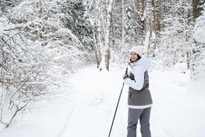 sciatore una donna con una giacca a membrana con bastoncini da sci in mano con la schiena sullo sfondo di una foresta innevata. sci di fondo nella foresta invernale, sport all'aria aperta, stile di vita sano. foto