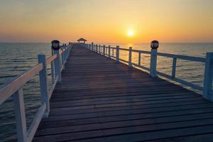 vista del ponte di legno che si protende nel mare al tramonto foto