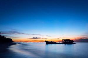 l'immagine di un peschereccio naufragato in riva al mare al tramonto. foto