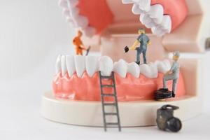 persone in miniatura per riparare un dente o un lavoratore di piccola figura che pulisce il modello di dente come medico e sanitario. foto