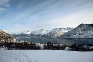 scenario della catena montuosa della neve e del villaggio norvegese sulla costa in inverno all'isola di senja foto