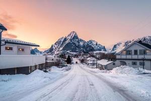 casa innevata con strada circondata da montagne al tramonto foto