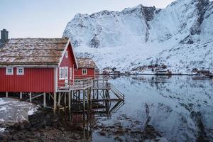 cottage rosso sulla costa nel villaggio di pescatori con la montagna di neve alle isole lofoten foto