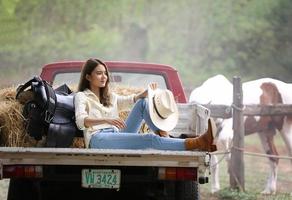 modello di cowgirl in posa in fattoria. un ritratto di una giovane e bella cowgirl appoggiata a un muro in una stalla in fattoria. foto