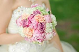 bouquet da sposa con fiori rosa e pesca nelle mani della sposa. garofano verde, rosa viola, peonia bianca foto