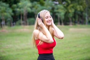 bella donna bionda in piedi mentre si ascolta musica in cuffia al parco. foto