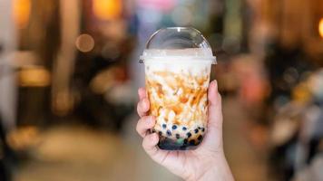 La giovane ragazza sta tenendo e mostrando una tazza di tè al latte con bolle di tapioca aromatizzato allo zucchero di canna nel mercato notturno di Taiwan sfondo, primo piano, bokeh foto