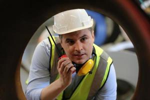 ingegnere industriale maschile che indossa un casco di sicurezza mentre si trova in una fabbrica industriale pesante. la manutenzione cercando di lavorare su macchinari industriali e controllare l'installazione del sistema di sicurezza in fabbrica. foto