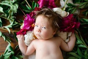 una bambina di due mesi giace su un tavolo con delle peonie. foto