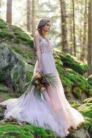 sposa felice in un abito da sposa rosa. la ragazza tiene in mano un bouquet da sposa. cerimonia di matrimonio in stile boho nella foresta. foto