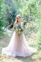 sposa felice in un abito da sposa rosa. la ragazza tiene in mano un bouquet da sposa. cerimonia di matrimonio in stile boho nella foresta. foto