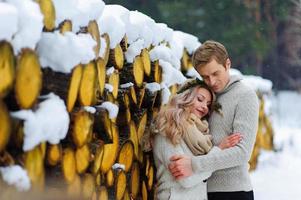 lo sposo bacia la sua sposa sulla tempia. sposi novelli con bouquet si siede sulla neve sullo sfondo di legno. matrimonio invernale foto