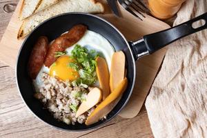 colazione all'inglese con uovo fritto con carne di maiale macinata e salsiccia servita in padella foto