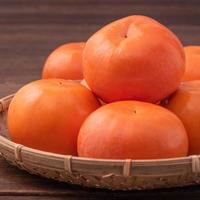 fresco, bel colore arancione cachi cachi sul setaccio di bambù su un tavolo di legno scuro. frutta stagionale e tradizionale del capodanno lunare cinese, primo piano. foto