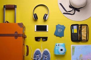 valigia arancione piatta con accessori da viaggio su sfondo giallo. concetto di viaggio foto