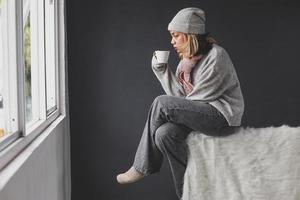 ragazza sola che guarda fuori attraverso la finestra in inverno mentre si gusta una tazza di caffè foto