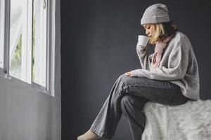 ragazza sola seduta e bere una tazza di caffè davanti alla finestra nella stagione invernale foto