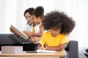 ritratto di felice giovane famiglia afroamericana con bambini piccoli sedersi rilassarsi sul divano coccole, sorridente genitori neri riposano sul divano abbraccio bambini in età prescolare che posano per una foto a casa insieme