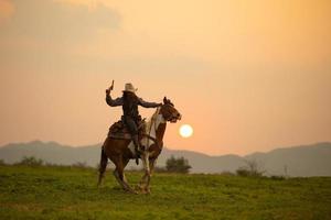 cowboy a cavallo contro un bel tramonto, cowboy e cavallo alle prime luci, montagna, fiume e stile di vita con sfondo di luce naturale foto