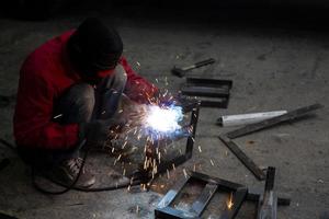 saldatore usato mola su acciaio in fabbrica con scintille, processo di saldatura presso l'officina industriale, mani con strumento nel telaio. foto