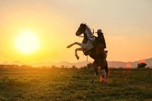 cowboy a cavallo contro un bel tramonto, cowboy e cavallo alle prime luci, montagna, fiume e stile di vita con sfondo di luce naturale foto
