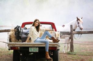 modello di cowgirl in posa in fattoria. un ritratto di una giovane e bella cowgirl appoggiata a un muro in una stalla in fattoria. foto