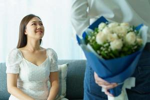 le giovani coppie asiatiche felici in San Valentino o anniversario stanno insieme, l'uomo dà e sorprende sua moglie un bouquet nel loro giorno di San Valentino o anniversario. marito e moglie che festeggiano a san valentino. foto