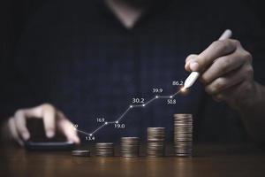 commerciante che scrive un grafico crescente sulle monete che si impilano per la crescita del profitto dell'investimento e il concetto di risparmio. foto