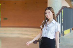 la bella studentessa asiatica della giovane donna sta sorridendo e sta esaminando la macchina fotografica nella priorità bassa dell'università foto