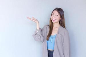 bella giovane donna asiatica con lunghi capelli castani in una camicia blu sta recitando a mano mostra come presentare qualcosa sullo sfondo. foto