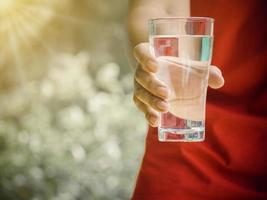 il giovane tiene il vetro con acqua pura su sfondo chiaro. concetto di salute, sete, calore e cure di bellezza. foto