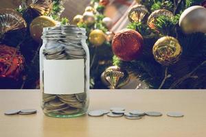 soldi nella bottiglia di vetro con la sfocatura dello sfondo dell'albero di Natale decorato foto