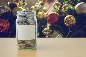 soldi nella bottiglia di vetro con la sfocatura dello sfondo dell'albero di Natale decorato foto