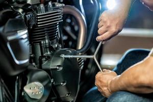 meccanico che utilizza una chiave inglese e una presa sul motore di una motocicletta in garage .manutenzione, riparazione moto concetto .messa a fuoco selettiva foto