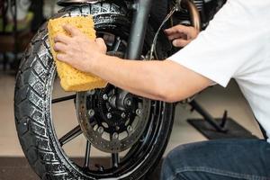 uomo che lava la motocicletta o lo scooter e spruzza schiuma di neve sulle ruote dei pneumatici. manutenzione del ripristino dei pneumatici, riparazione del concetto di motocicletta in garage. messa a fuoco selettiva foto