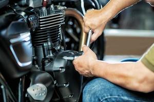 meccanico che utilizza una chiave inglese e una presa sul motore di una motocicletta in garage .manutenzione, riparazione moto concetto .messa a fuoco selettiva foto