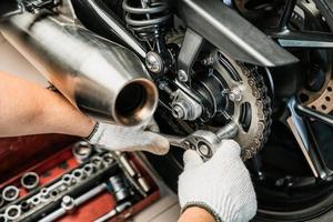 meccanico che utilizza una chiave e una presa sul pignone della motocicletta. concetto di manutenzione e riparazione nel garage della motocicletta. messa a fuoco selettiva foto