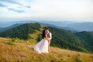 elegante giovane sposa e sposo stanno in barca su sfondo cloude cielo mare e montagne del montenegro foto