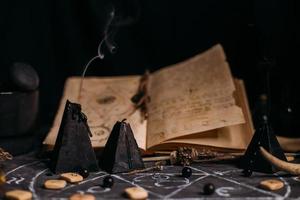 apri il vecchio libro con incantesimi, rune, candele nere sul tavolo delle streghe. concetto occulto, esoterico, divinatorio e wicca. foto