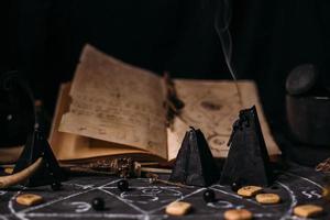 apri il vecchio libro con incantesimi, rune, candele nere sul tavolo delle streghe. concetto occulto, esoterico, divinatorio e wicca. foto