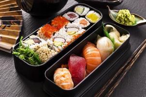 pasto giapponese in una scatola di bento con sushi e involtini di riso su un tavolo di legno nero foto