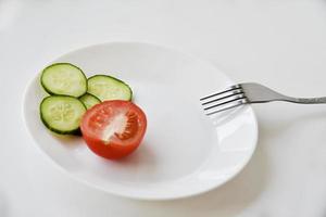 cetriolo e pomodoro interi e affettati su un piatto e una forchetta bianchi foto