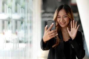 giovane donna di affari asiatica bella sorridente affascinante avendo una videochiamata con uno smart phone in ufficio foto