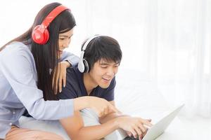 una felice giovane coppia asiatica è seduta a letto e si diverte a guardare film su un laptop su uno sfondo bianco. foto