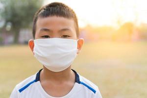 un ragazzo asiatico indossa una t-shirt bianca e indossa una maschera facciale di colore bianco su uno sfondo sfocato naturale all'alba. foto