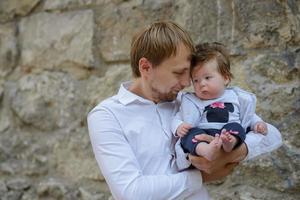 Ritratto di giovane padre che tiene piangendo bambina su un muro di mattoni bianchi foto