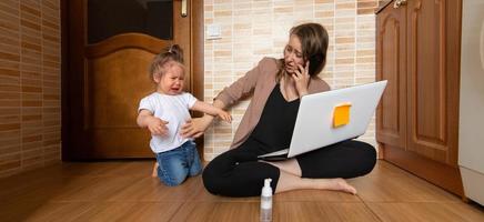 la giovane bella madre sta cercando di lavorare a distanza. la sua piccola figlia la infastidisce. foto