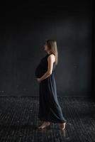 ritratto di una ragazza incinta contro un muro nero foto