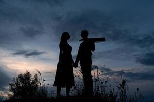 sagoma di una coppia innamorata ad un appuntamento. l'uomo tiene la mano della ragazza. il tizio in granchi ha una chitarra. girato al tramonto. foto